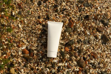 Boş bir nemlendirici tüpünün beyaz modeli ya da plajın yakınındaki ıslak deniz kabuklarında yüz derisi için güneş kremi. Güzellik ürünleri ve doğal kozmetik kavramı