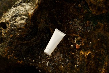 Deniz kenarındaki ıslak bir taşın üzerindeki yüz derisi için nemlendirici ya da güneş kremi tüpünün beyaz modeli. Doğal kozmetik ürünleri, güzellik ürünleri kavramı