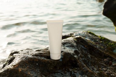 Beyaz nemlendirici krem tüpü ya da vücut ve yüz için losyon denizin arka planında ıslak bir taşın üzerinde. Doğal kozmetik, güzellik ürünleri ve estetik konsepti