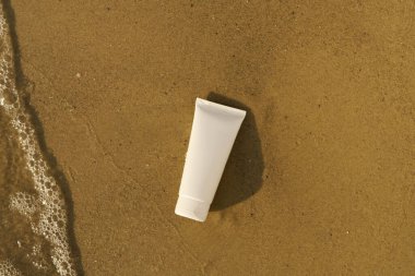Güneşten korunmak için beyaz, boş bir krem tüpü ya da ıslak kumdaki deriyi deniz suyuyla nemlendirmek için. Güneş kremi, plajda dinlenme, yaz kozmetik konsepti..