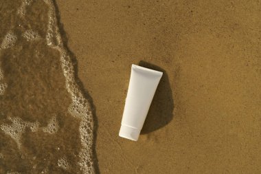 Boş bir ceset kavanozunun beyaz bir modeli ya da ıslak kumun üzerinde deniz suyu dalgası ile yüz kremi. Güneş koruması, cilt nemlendirici, doğal kozmetik konsepti