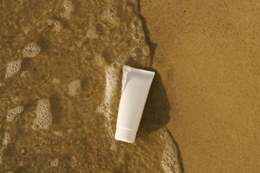 Islak kumun üzerinde bir tüp güneş kremi, losyon ya da nemlendirici ve akmakta olan bir deniz suyu. Vücut bakımı konsepti, doğal kozmetik.