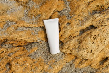 Beyaz mocap tüp vücut kremi ya da deniz kenarındaki kumlu kireç taşı üzerinde yüz. Deriyi besleyip nemlendirmek için doğal kozmetik ürünleri ve eser miktarda elementler.