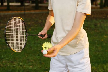 Genç bir kadın açık havada badminton oynarken elinde raketle servis yapacak. Açık hava sporları, aktiviteler, boş zaman konsepti.