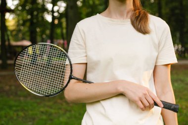 Elinde badminton raketi tutan tişörtlü genç bir kadının yakın çekimi. Açık hava sporları, rekabet ve eğlence kavramı