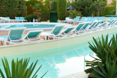Bir lunaparktaki ya da otelin yakınındaki bir havuzda mavi güneşli yatakların ve mavi suyun yatay görüntüsü. Yaz tatili, tatil ve güneşin altında iyi vakit geçirme kavramı.