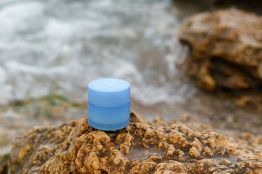 Mavi yüz kremi kavanozu deniz suyundaki sarı kireç taşının üzerinde. Yüz ve göz çevresi için cilt bakımı kavramı