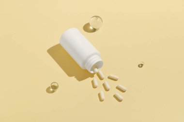 Beyaz maket kavanozu ve sarı izole arka plana dökülen haplar. Doğal beslenme takviyeleri, eczane ve sağlık hizmetleri kavramı.