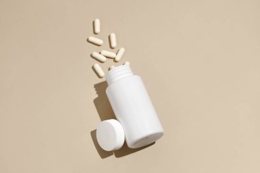Bej izole edilmiş arka planda dağınık hap kapsülleri olan beyaz model kavanoz. Eczane, sağlık, tıbbi ve beslenme malzemeleri kavramı. Tasarımın için resim