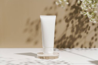 Beyaz makyaj tüpü, doğal yüz kremi, cam kaidesi, bej ve çiçek arkaplanı. Kozmetik ürünler, estetik, güzellik ürünleri konsepti.