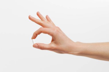 Beyaz izole edilmiş arka planda parmakları olan beyaz hap kapsülünü tutan kadın eli. Sağlık, beslenme desteği, hastalık tedavisi ve eczane kavramı.