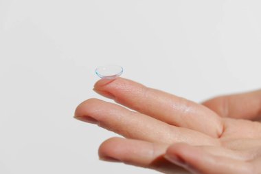 Finger of female hand holding blue transparent contact lens on white isolated background. Vision improvement concept, ophthalmology, myopia. clipart
