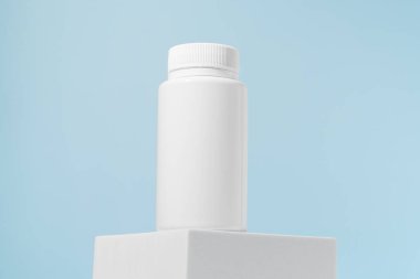 Beyaz hap kavanozu mavi arka planda bir kaide üzerinde. Eczane, ilaç, sağlık ve beslenme desteği kavramı.