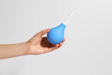 Bir kadın eli gri arka planda küçük bir kauçuk mavi lavman tutar. İlaç konsepti, eczane, vücudu temizlemek. Tasarımın için resim