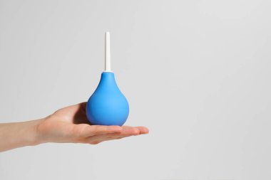 Bir dişi el, gri izole bir arka planda avucunun içinde küçük mavi bir lavman tutar. Vücudun eczacılık, ilaç, sağlık ve detoksifikasyon konsepti