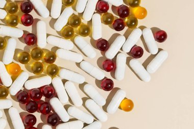 Bej arka planda kırmızı, sarı ve beyaz kapsül hapları. Sağlık tedavisi, vitaminler ve besin takviyeleri kavramı.