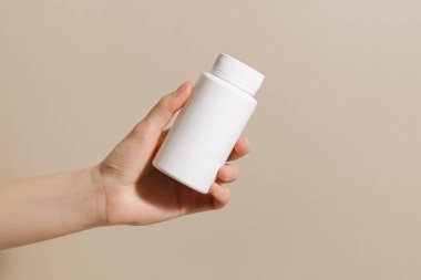 Bej izole arka planda beyaz hap kavanozunu tutan bir kadın. Eczane, ilaç, doğal beslenme malzemeleri kavramı..