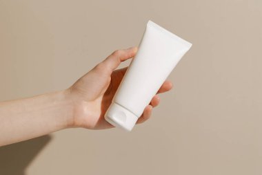 Bej izole arka planda beyaz krem tüp modeli tutan bir kadın. Güzellik konsepti, bakım kozmetik, günlük rutin.