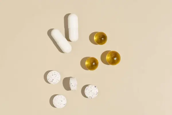 Beyaz ve sarı kapsül hapları, bir bardak suyla izole edilmiş bej arka plan. Eczane kavramı, günlük ilaç alımı, sağlık ve güzelliği iyileştirmek için vitaminler..