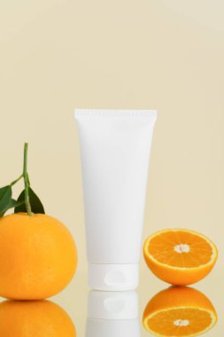 Beyaz yüz kremi tüpünün dikey modeli ve portakallar bej izole arka planda aynaya yansıyor. Cilt için güzellik ürünleri, kolajen ve vitamin kavramı