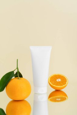 Bej izole edilmiş arka planda portakallı beyaz bir krem tüpünün dikey görüntüsü. Doğal kozmetik ürünleri ve cilt bakımı konsepti