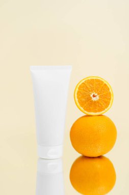 Beyaz yüz kremi tüpünün dikey modeli ve portakallar bej izole arka planda aynaya yansıyor. Nemlendirme ve cilt bakımı kavramı, güzellik ürünleri.