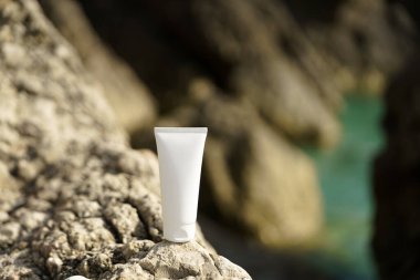 Deniz kenarındaki bir kayanın üzerindeki yüz ya da vücut kremi tüpünün beyaz bir modelini yakın plan çek. Cilt bakımı, nemlendirici ve güneş koruması için doğal güzellik ürünleri kavramı. Tasarımın için resim