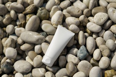 Deniz suyunun yanındaki ıslak çakıl taşı plajında yakın plan beyaz krem tüpü. Güneş koruması için doğal güzellik ürünleri kavramı spf, nemlendirici ve rahatlatıcı cilt.