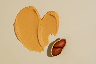 Kalp şeklinde kremalı fındık ezmesi ve bej izole arka planda fıstık ezmesi. Protein kaynağı, sağlıklı atıştırmalık, fıstık ezmesi kavramı..