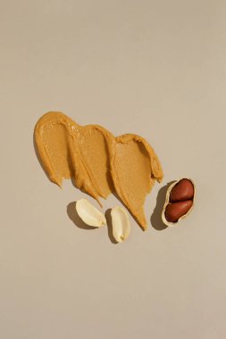 Kahverengi fıstık ezmesinin krema lekesi ve bej izole arkaplanda yer fıstığının dikey görüntüsü. Protein besin konsepti, doğal bileşenler.