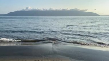 Düz pantolonlu ve beyaz tişörtlü genç bir kadın rüyasında deniz kıyısının arka planındaki kumda yürüyor. Yalnız zaman geçirme kavramı, doğayla bütünlük, yaşam tarzı, tatil