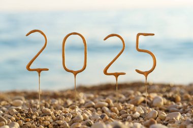 Deniz suyunun arka planında 2025 yıllık çakıl taşları ve sahilde gün batımına yakın çekim. Mutlu yıllar, başarı ve refah dileklerim, tebrikler, kutlamalar, tebrik kartları