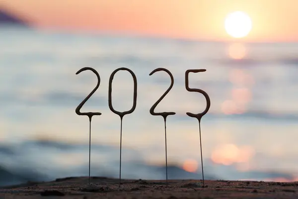 2025 numara, batan güneşin ışıldayan mavi suyunun arka planında ve sahilde gün batımında. Yeni yıl ve Noel 'i kutlamak, başarı ve refah dilemek.