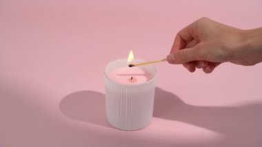 Genç bir kadının eli pembe bir mumu pembe izole bir arka planda yanan bir kibritle yakar. Samimiyet, dekorasyon, kutlama, meditasyon ve rahatlama kavramı.