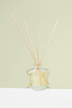Dikey görüntü aroması yayılmış şeffaf cam kavanoz taze kokusu ve yeşil izole arkaplanda çiçekler. İçinde rattan çubuklar olan ev parfümü şişesi. Basit ev dekorasyonu fikri