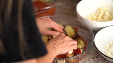 Genç bir kadın, mutfakta klasik parmesan peynirini hazırlamak için bir tabağa kızarmış ve dilimlenmiş patlıcan koyuyor. Ev yemeği, sağlıklı beslenme, taze sebzeler.