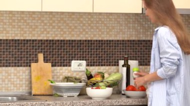 Genç bir kadın mutfakta dururken tuzluk ile salatayı tuzluyor. Ev yemeği, sağlıklı beslenme ve beslenme.