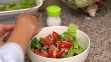 Genç bir kadın mutfakta dururken salataya balkabağı tohumları serpiyor. Ev yemeği, sağlıklı beslenme ve beslenme.