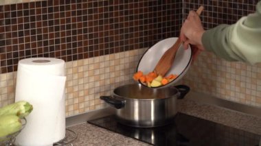 Genç bir kadın çorba yapmak için ocağa sebze koyar ve mutfakta karıştırır. Ev yemeği, sağlıklı beslenme ve beslenme.
