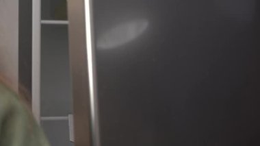 Genç bir kadın buzdolabını soğuk tutmak ve bozulmasını önlemek için tencereye tabak veya çorba koyar.