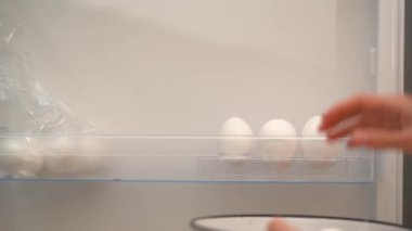 Genç bir kadının eli buzdolabının kapısından beyaz yumurtaları alır ve kapatır. Evde yemek pişirmek, soğukta yemek depolamak....