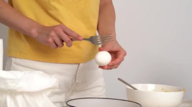 Sarı elbiseli genç kadın bir yumurta kırıyor ve mutfak masasında ev yapımı hamur işleri yaptığı için derin bir tabağa döküyor. Zaman geçirme kavramı, yemek pişirme hobisi