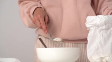 Genç bayana yakın çekim için kaşık kaşık ile kağıt torbadan un alın ve onu kaseye dökün, hamur yoğurarak daha fazla pasta veya kurabiye hazırlamak için. Yemek pişirme, mutfak hobisi malzemesi kavramı