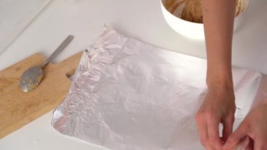 Beyaz mutfak masasındaki genç kadın folyoyu yırtıyor ve buzdolabında depolamak için bir parça hamur sarıyordu. Evde yemek pişirme malzemesi kavramı, aşçılık hobisi