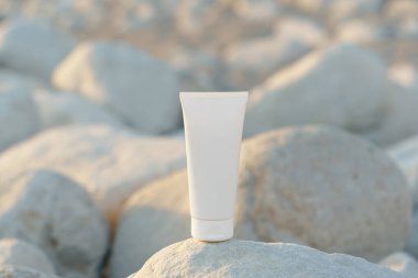 Sahildeki deniz kenarındaki çakıl taşlarının üzerinde batan güneşin aydınlattığı beyaz model kremi kapat. Güneş ve uva, cilt bakımı, güzellik ve estetikten korunma kavramı.