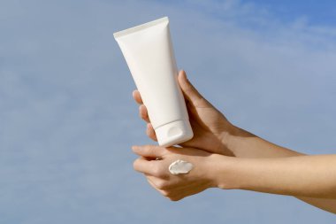 Lekeli kadın eller mavi arka planda beyaz model tüp tutuyor. Güzellik ürünleri, yüz ve vücut bakımı kavramı