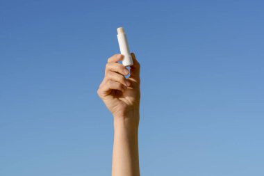 Mavi gökyüzü arka planında beyaz dudak kremi tutan bir kadın. Nemlendirici ve pürüzsüz dudak derisi, ruj ve nazik bakım kavramı