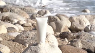 Deniz dalgalarının arka planında bir kayanın üzerinde duran bir krema kavanozunun beyaz modeli. Cilt için güneş kremi kavramı, nemlendirici, vücut bakımı, güzellik ürünleri
