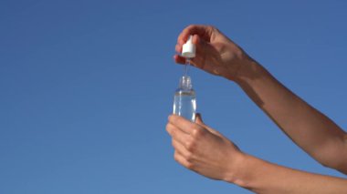 Dişi eller cam bir kavanoz serum açar ve mavi gökyüzü arka planındaki deriye pipet kutusundan serum uygular. Güzellik ve estetik ürünleri kavramı, yüzü nemlendirici ve besleyici