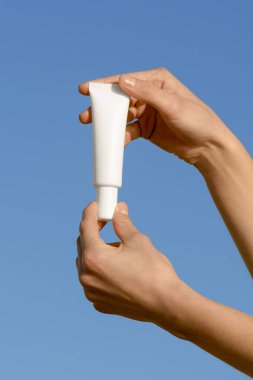 Mavi arka planda beyaz boş yüz kremi ya da serum tutan kadın ellerinin dikey görüntüsü. Cilt bakımı, güzellik ve estetik ürünleri için doğal kozmetik kavramı. Tasarımın için bir model